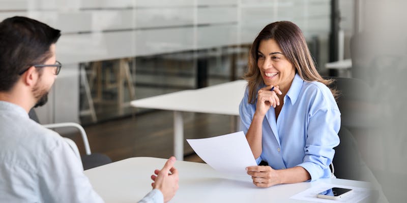 Une femme sourit à son interlocuteur avec un papier dans la main.